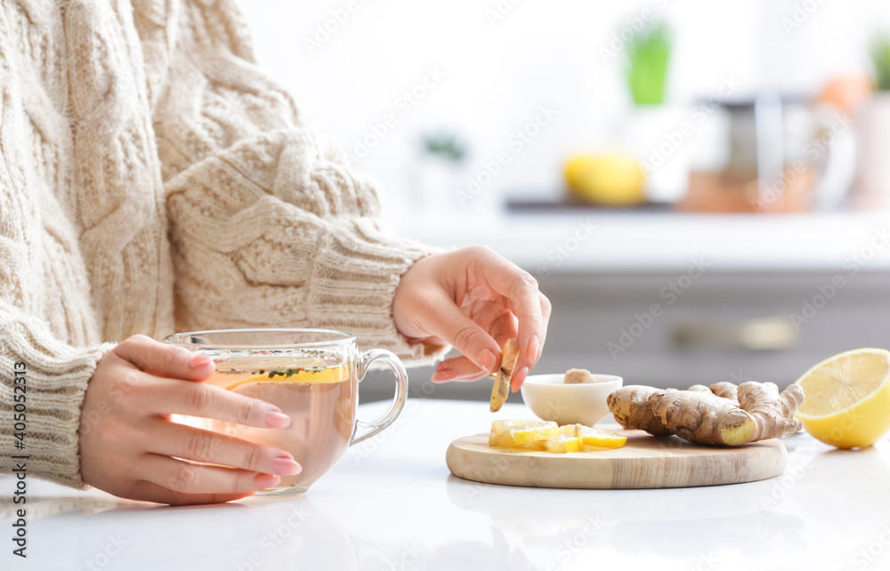 Woman making healthy tea with ginger and lemon in kitchen
