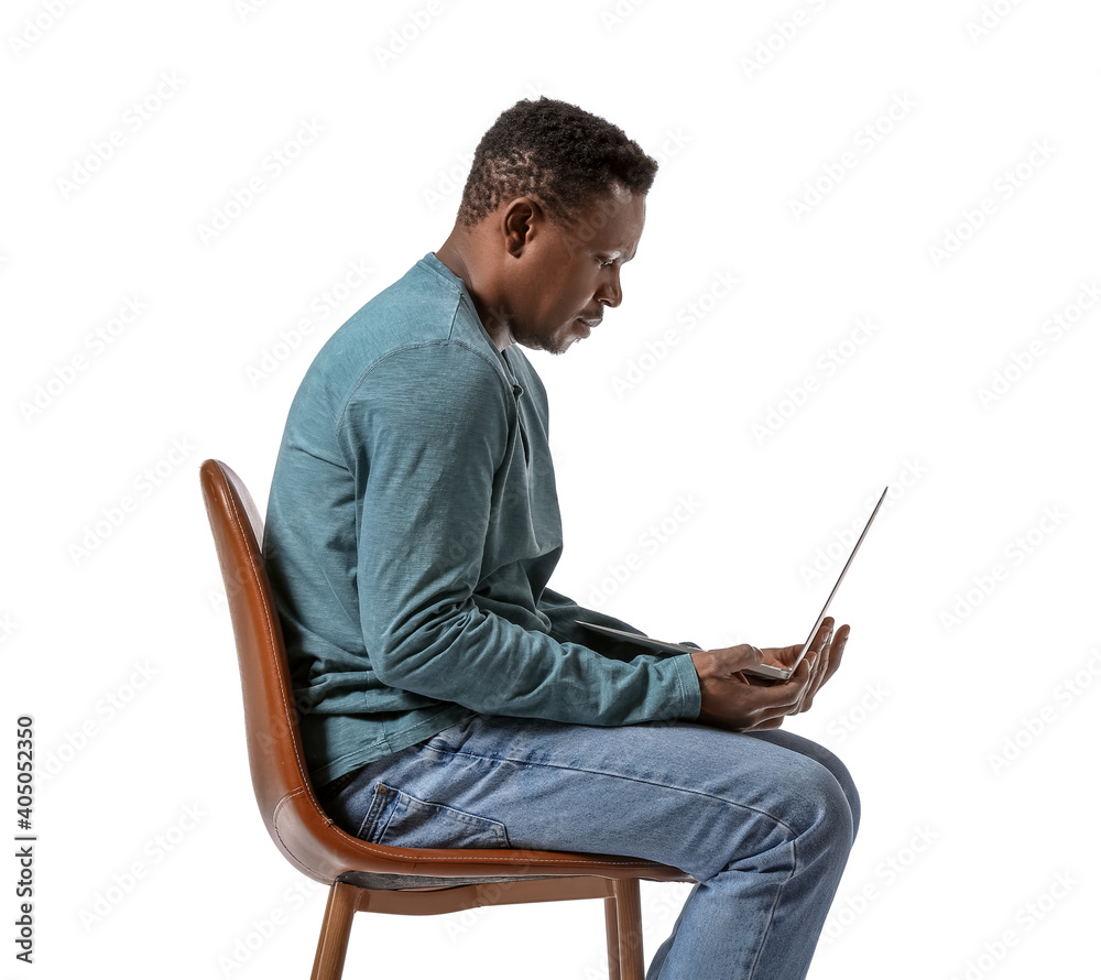Hunchbacked African-American man with laptop sitting on chair against white background