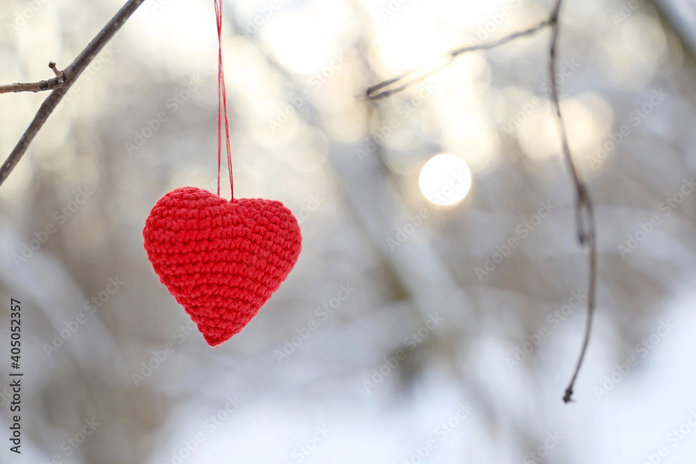 Valentine heart in winter forest against the sun. Red knitted heart hanging on a branch, symbol of romantic love, background for snow holiday Valentine heart in winter forest against the sun. Red knitted heart hanging on a branch, symbol of romantic love, background for snow holiday