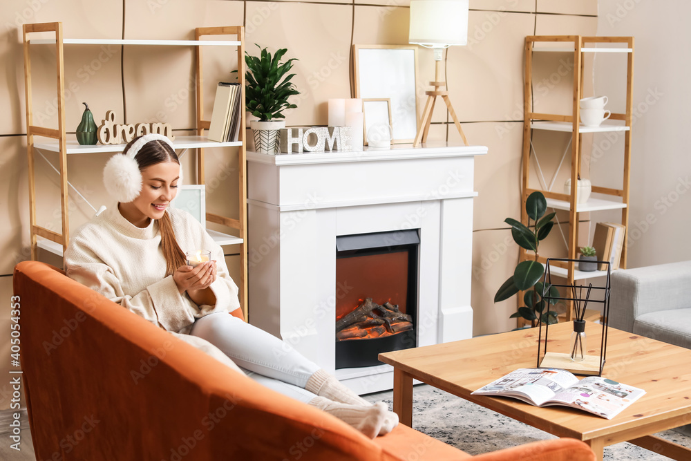 Young woman with candle near fireplace at home - obrazy, fototapety, plakaty 