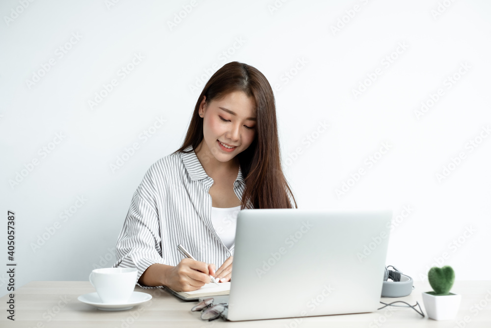 Asian female college students study online at home, enjoy extra lessons, watch videos, and take notes from a digital laptop, do homework by looking at the screen while sitting at a desk at home Asian female college students study online at home, enjoy extra lessons, watch videos, and take notes from a digital laptop, do homework by looking at the screen while sitting at a desk at home