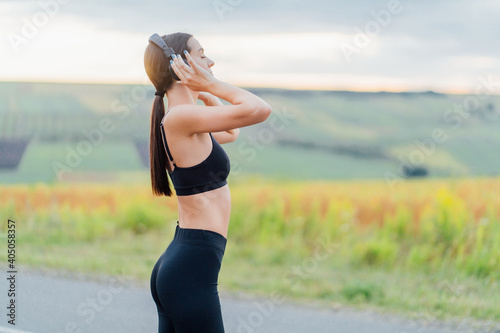 Athletic girl listens to music during training and enjoys the dawn