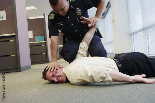 Police officer holding beat up businessman on floor in office