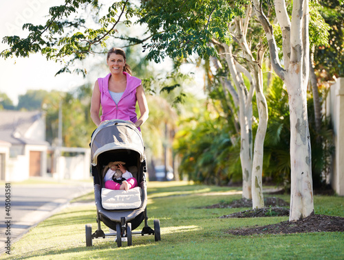 Mother in exercise gear pushing baby in stroler along suburban street photo
