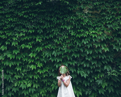 Girl hiding her fave with green leaf and standing near tree