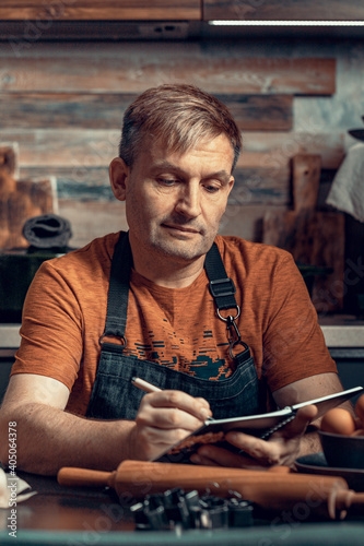 Caucasian man in a apron writes the recipe into the diary. Life style photography. Home kitchen. Vertical shot