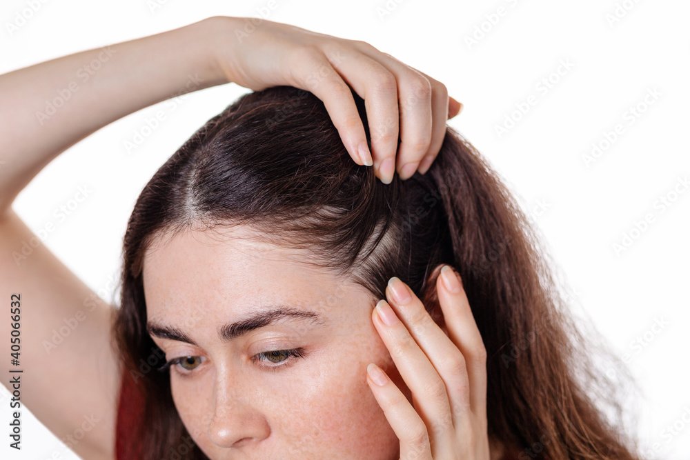 Fototapeta premium A woman examines the parting in her hair, pushing the strands apart with her hands. The view from the top. White background. the concept of dandruff and lice