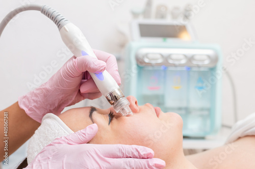 Beauty salon. The cosmetologist performs a water peeling procedure on the client's cheeks. Side view. Close up of face and device. Professional skin care and beauty concept