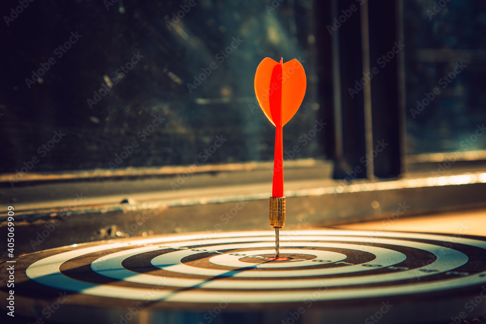 Dart arrow hit on bulleyes of dartboard to represent that the business reached the target  with dark tone picture style. Target and goal as concept.