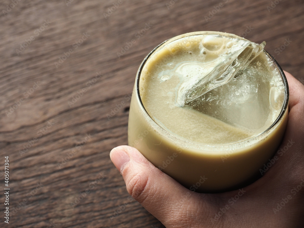 hand holding iced green tea on wooden table hand holding iced green tea on wooden table