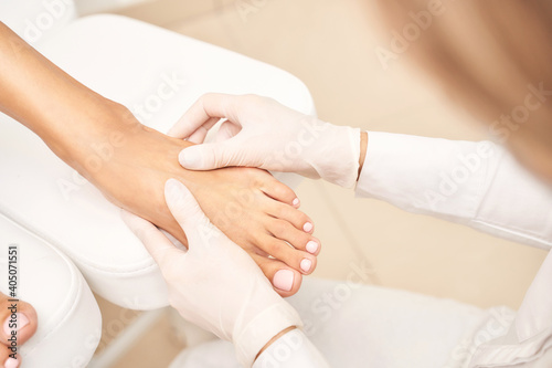 Pedicure nail spa procedure. Foot manicure. Salon master. Polish woman leg. Hands in gloves. Light background. Massage service. Healthy toe cleaning. Pink pastel color. Dermatology cream photo