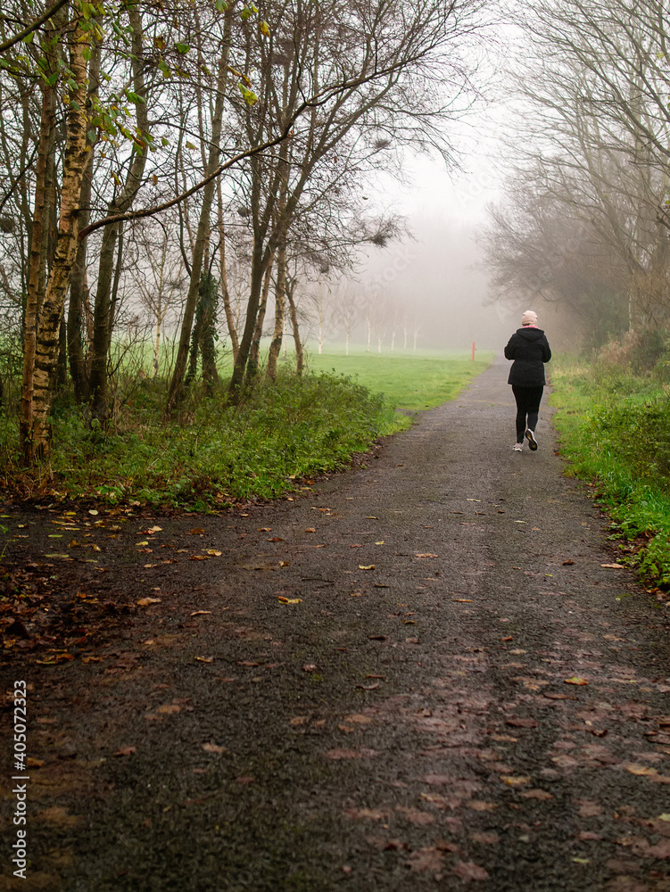 Athletic woman jogging on a small path in a park in the morning. Fog in the background, Vertical image. Selective focus. Physical activity and fitness concept Athletic woman jogging on a small path in a park in the morning. Fog in the background, Vertical image. Selective focus. Physical activity and fitness concept