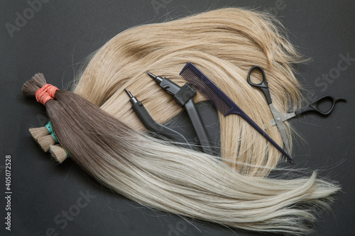 a large strand of hair with a thin comb-scissors device for encapsulating on a black background. 