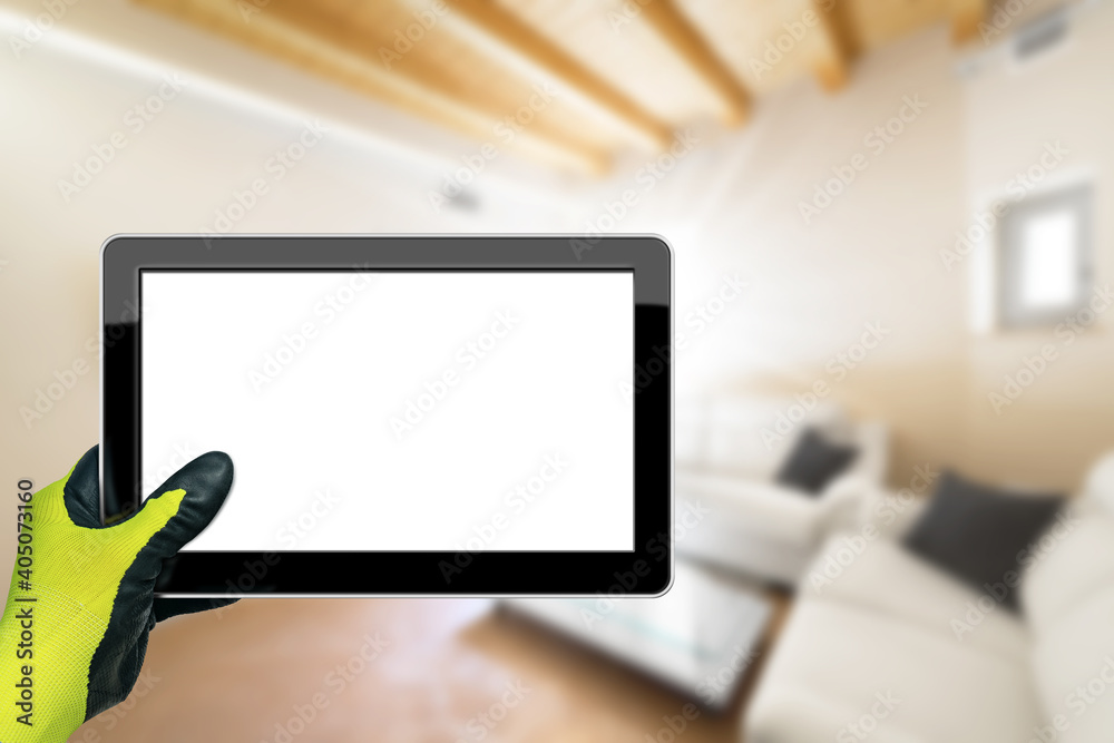 Hand with work glove holding a blank digital tablet with a blurred living room in the background. Hand with work glove holding a blank digital tablet with a blurred living room in the background.