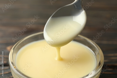 Spoon and bowl with condensed milk on wooden background