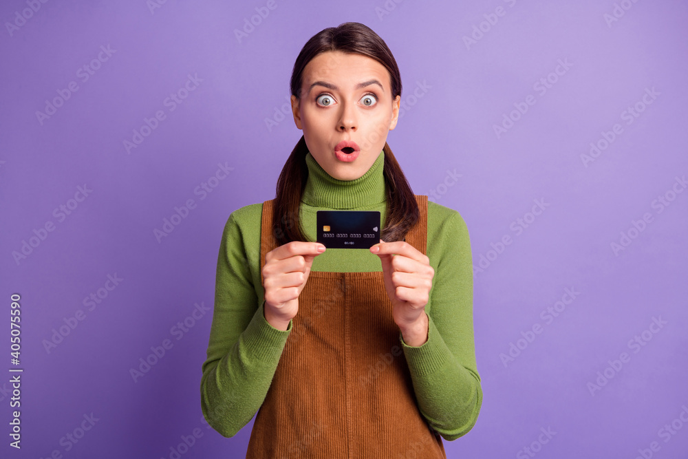 Portrait of lovely amazed funky girl holding in hands bank card staring eyes isolated over bright violet color background Portrait of lovely amazed funky girl holding in hands bank card staring eyes isolated over bright violet color background