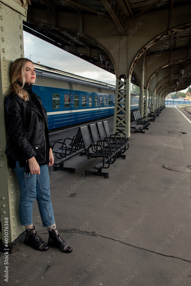 Young beautiful woman in a leather jacket on a perone next to the train at the railway station. Waiting for the train Vitebsk station St. Petersburg.