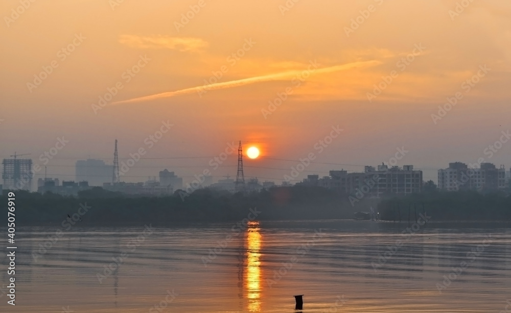 Beautiful sunrise view and reflection of sun in water with orange color sky and greenery in background .For wallpaper and templates at Gorai ,Mumbai