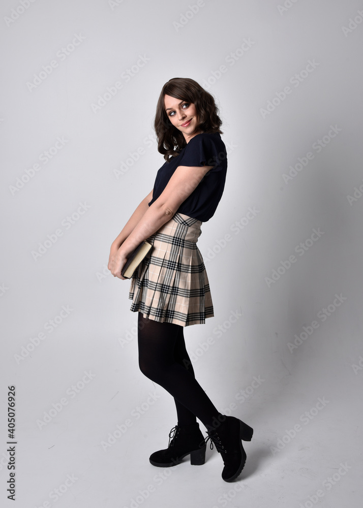 full length portrait of pretty brunette woman wearing tartan skirt and boots. Standing pose holding books against a studio background. full length portrait of pretty brunette woman wearing tartan skirt and boots. Standing pose holding books against a studio background.