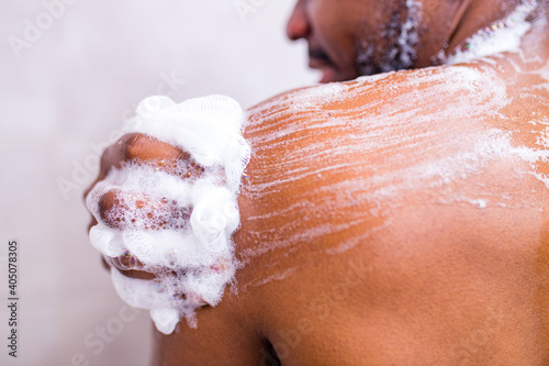 brazilian man washing body with shower sponge in white bathroom