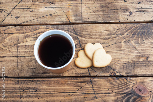 Black coffee in a paper cup and cookies in the shape of hearts on a wooden background. flat lay copy space, top view.