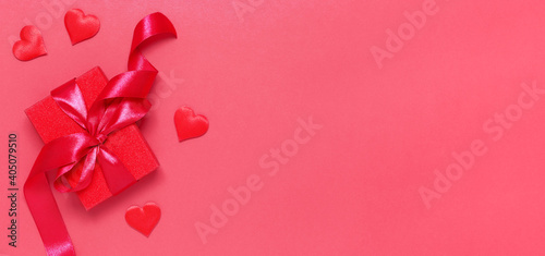 Red gift box tied with a ribbon with decorative hearts on a red background. Gift for Valentine's. Banner © Marina Kaiser