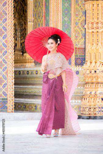 THAILAND, Beautiful woman in a pink Thai dress or a traditional Thai dress is spreading a red umbrella in a Thai temple.