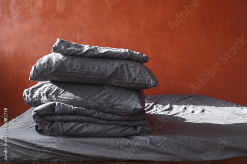 A stack of plain pillows, blankets on the bed. Gray linens on red wall background