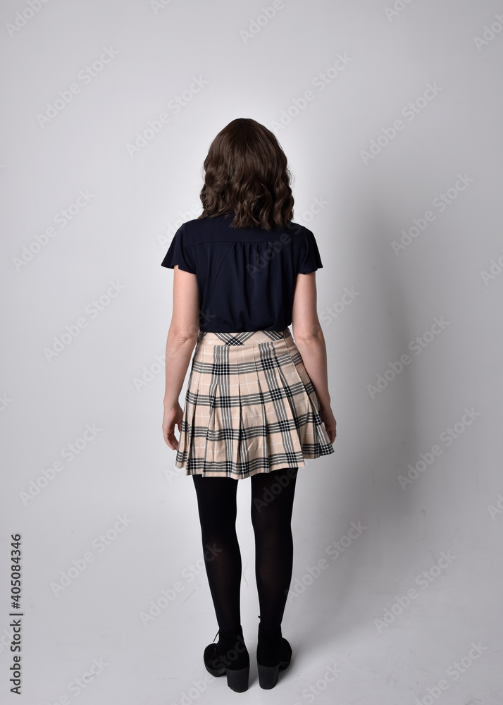full length portrait of pretty brunette woman wearing tartan skirt and boots. Standing pose with back to the camera against a studio background. full length portrait of pretty brunette woman wearing tartan skirt and boots. Standing pose with back to the camera against a studio background.
