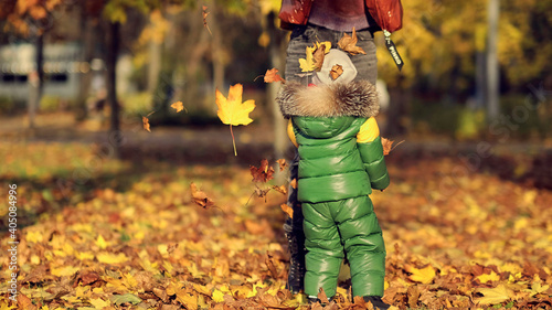 Mom and son throw autumn leaves in autumn park, family fun. family enjoying a walk in nature. happy motherhood concept.