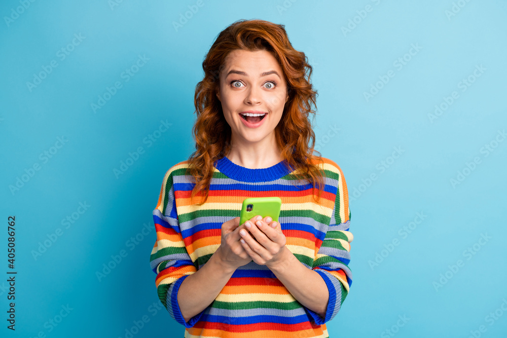 Photo of sweet surprised ginger woman wear colorful sweater holding modern device isolated blue color background Photo of sweet surprised ginger woman wear colorful sweater holding modern device isolated blue color background