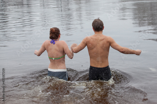 Woman and man entering the icy water of a winter river in water baptism in the Orthodox tradition. Dnieper. Kiev. Ukraine