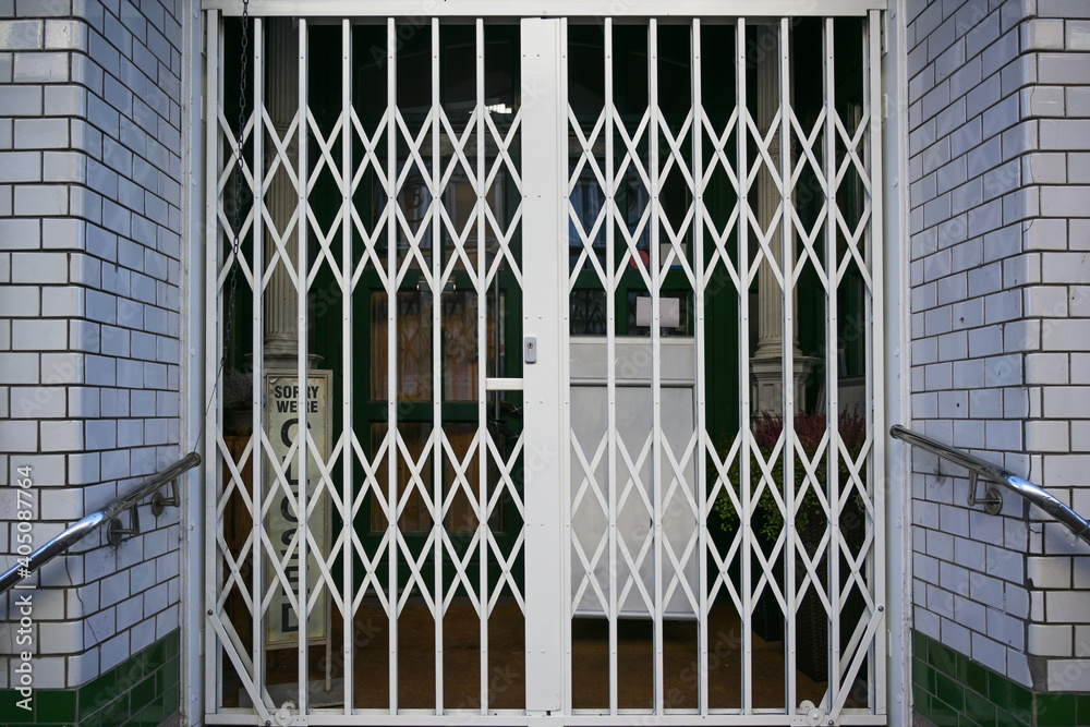 Shuttered security grille in front of a retail store, that had to close during the lockdown due to the coronavirus pandemic crisis with risk of infection with covid-19 - obrazy, fototapety, plakaty 