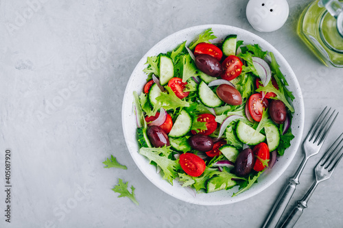 Healthy green salad with fresh tomato, cucumber, red onion, olives and lettuce in bowl