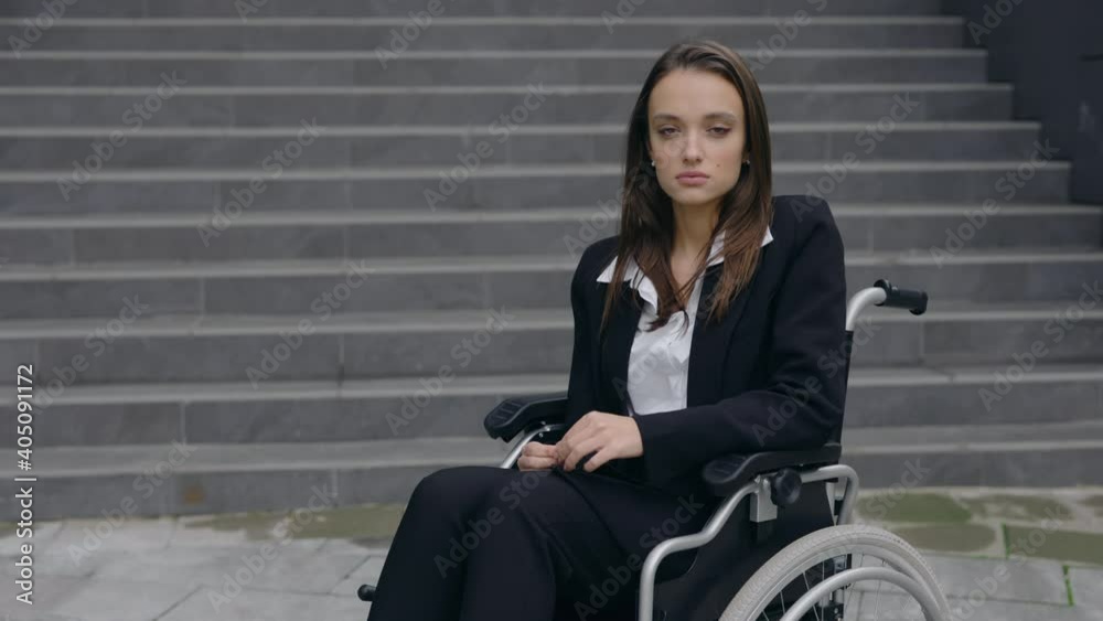 Crop view of handicapped beautiful businesswoman in suit sitting in wheelchair at street. Disabled young female person looking to camera outdoors. Concept of successful people. Crop view of handicapped beautiful businesswoman in suit sitting in wheelchair at street. Disabled young female person looking to camera outdoors. Concept of successful people.