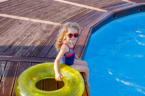 little girl in sunglasses and swimsuit  sitting by the pool in summer