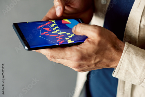 Closeup view of a businessman holding phone with graphs and diagrams on the screen, analyzing startup statistics, checking financial trade report presentation. A broker working with graphs on a device
