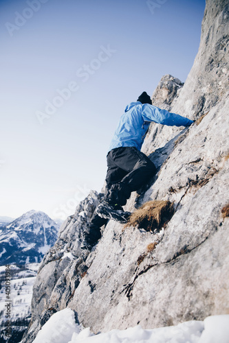 Sportlicher Alpinist klettert schneebedecktes Gestein und winterliches Gebirge entlang