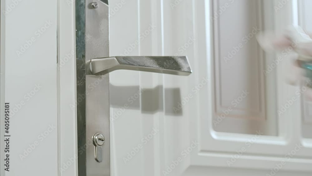 Woman in protective gloves spreading sanitizer on a door handle and wipe it with a special napkin. Protection from viruses in pandemic time even at home. Woman in protective gloves spreading sanitizer on a door handle and wipe it with a special napkin. Protection from viruses in pandemic time even at home.