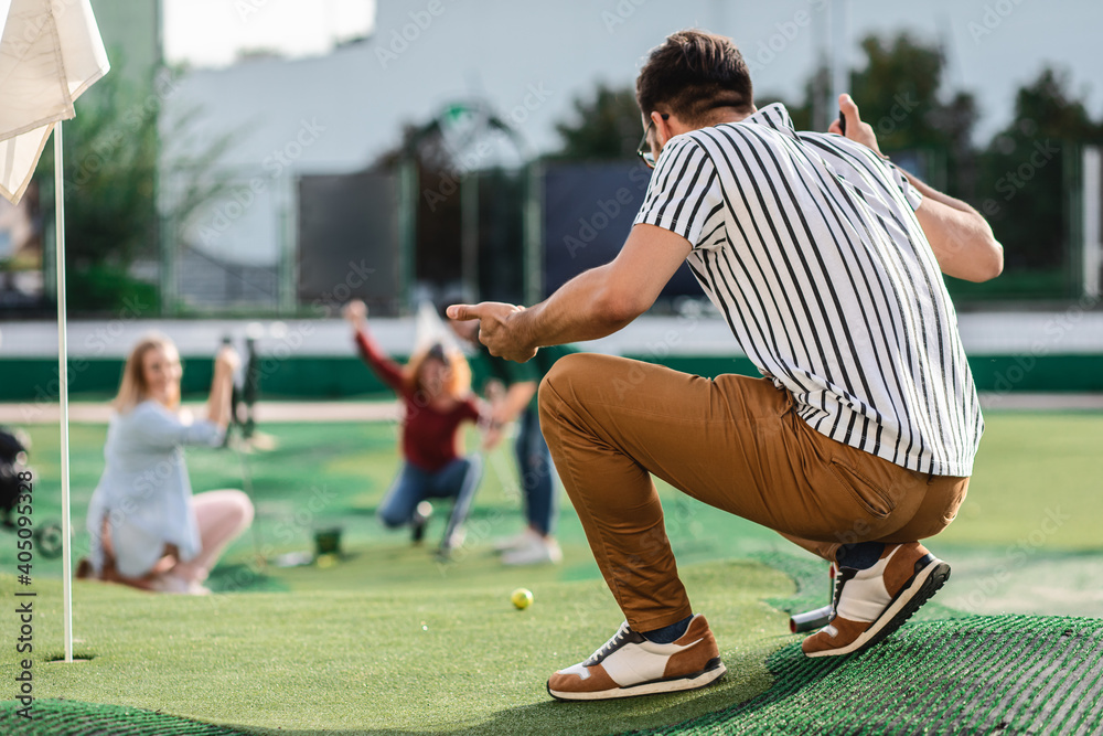 Fototapeta premium Group of smiling friends enjoying together playing mini golf in the city.