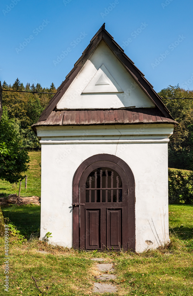 White colored chapel with wooden door, forest on the background and clear sky