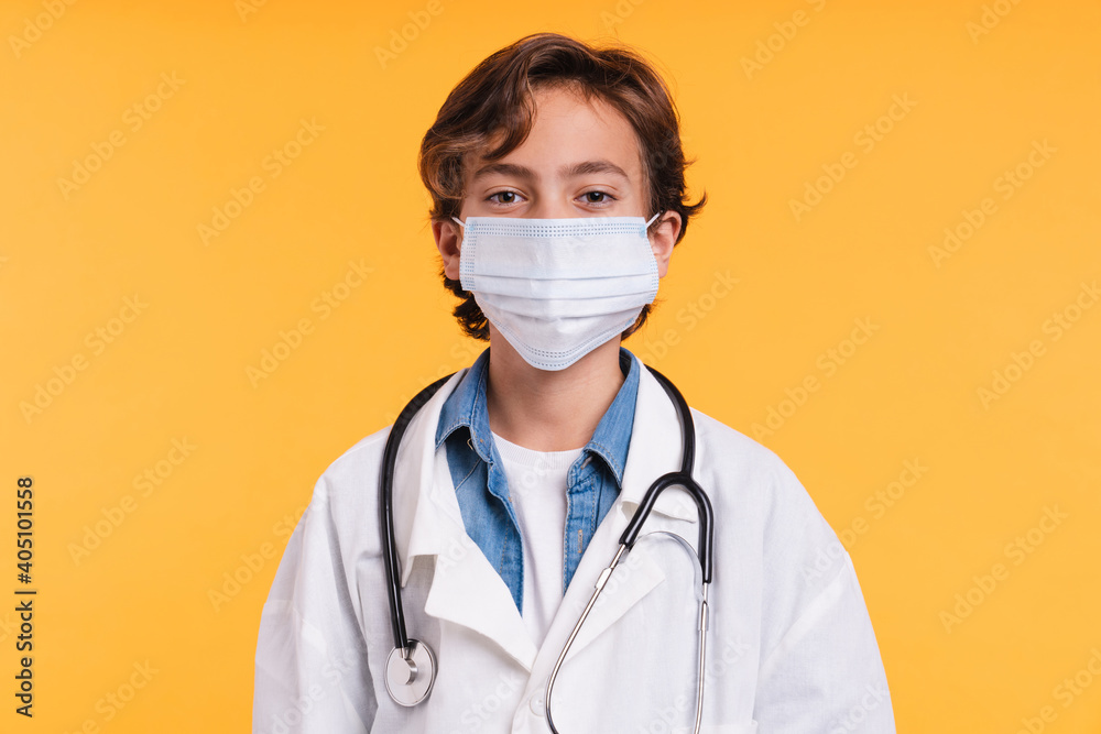 Close up portrait of young future doctor in medical coat with stethoscope in medical mask against coronavirus isolated over yellow background Close up portrait of young future doctor in medical coat with stethoscope in medical mask against coronavirus isolated over yellow background