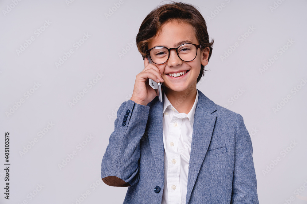 Cheerful smiling little boy talking on phone in formal clothes isolated over grey background Cheerful smiling little boy talking on phone in formal clothes isolated over grey background