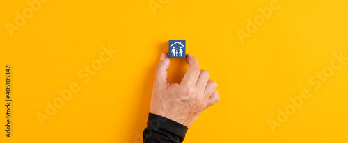 Male hand holds a blue wooden cube with a family in a house icon on yellow background. Home insurance and security