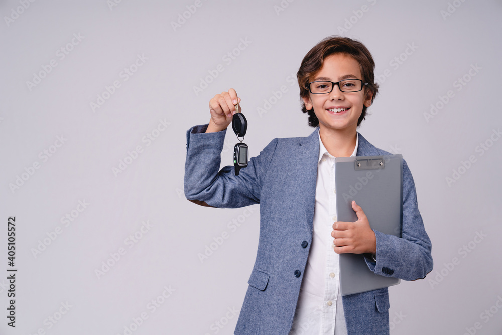 Clever young boy future estate agent holding a clipboard and keys isolated over grey background Clever young boy future estate agent holding a clipboard and keys isolated over grey background