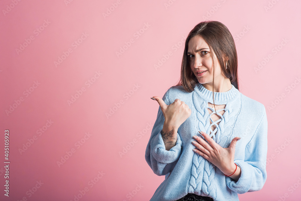Portrait of a brunette girl on a pink background who points her thumb to copyspace