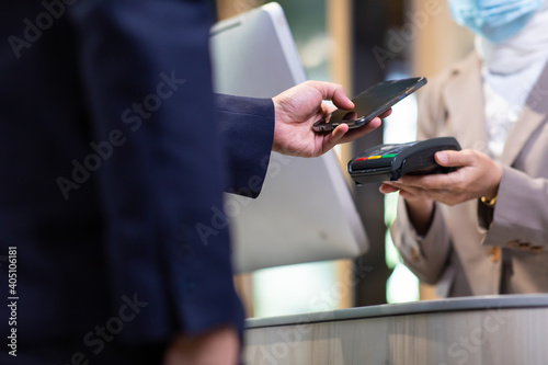 Female receptionist employee holding card reader machine on hand at checkout counter. Protective face mask during coronavirus and flu outbreak. Virus and illness protection