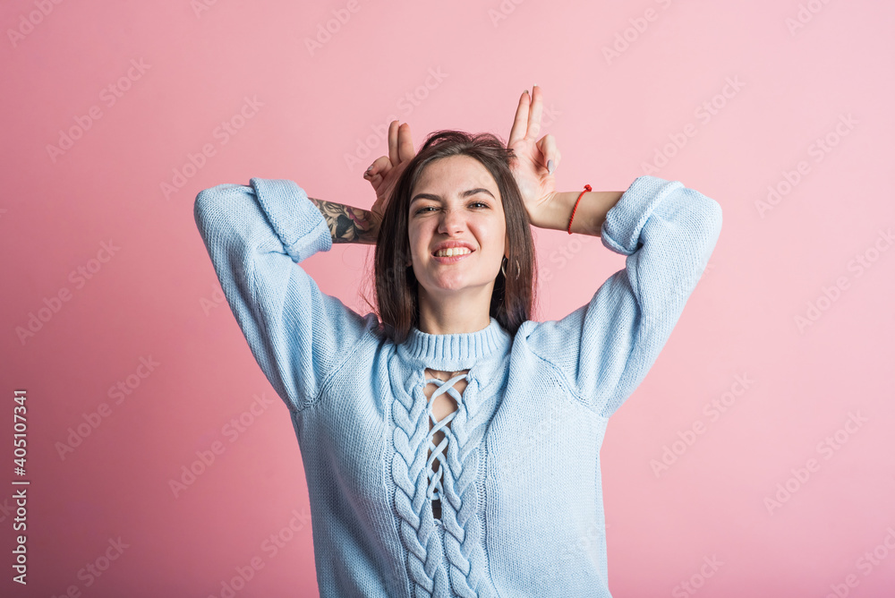 Happy brunette girl shows funny face with horns in studio on pink background