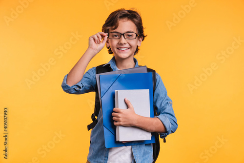 Clever young boy holding folders for studing at school isolated over yellow background photo