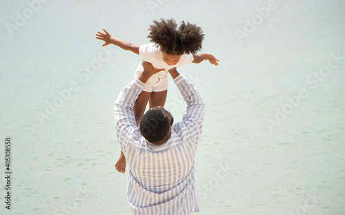 Father holding his daughter up high against sky. african american dady hug girl with sea background
